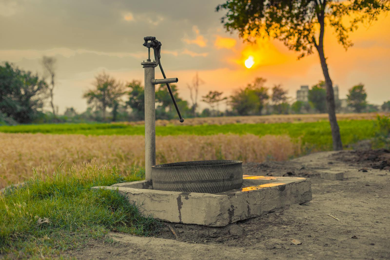A vintage water pump amidst picturesque fields at sunset, capturing rural tranquility.